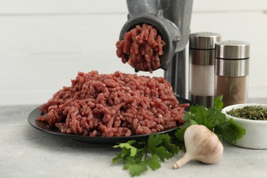 Photo of Mincing beef with manual meat grinder. Parsley, garlic and spices on grey table