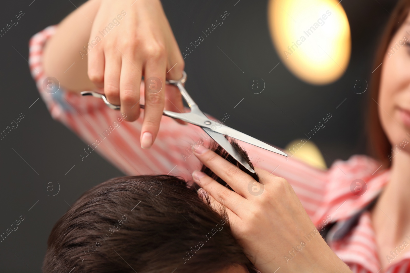 Photo of Barber making stylish haircut with professional scissors in beauty salon, closeup