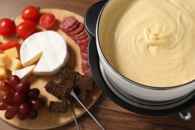 Photo of Fondue with tasty melted cheese, forks and different snacks on wooden table, above view