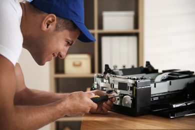 Repairman with screwdriver fixing modern printer in office