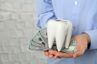 Photo of Woman holding ceramic model of tooth and dollar banknotes on light background, closeup. Expensive treatment
