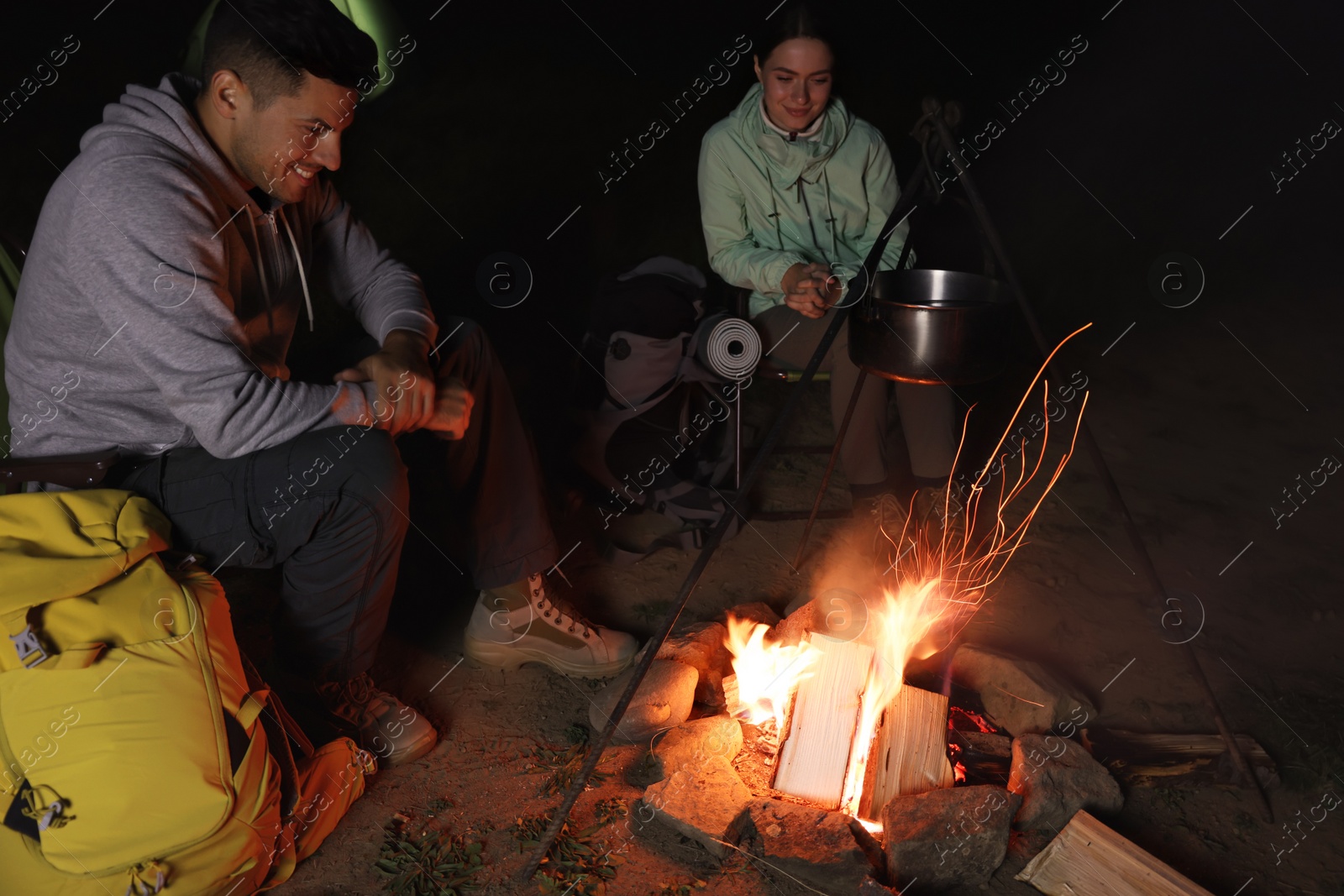 Photo of Couple sitting near bonfire in camp at night