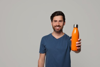 Man with orange thermo bottle on light grey background. Space for text