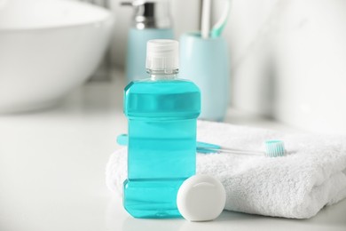 Photo of Mouthwash, toothbrush, towel and dental floss on white countertop in bathroom