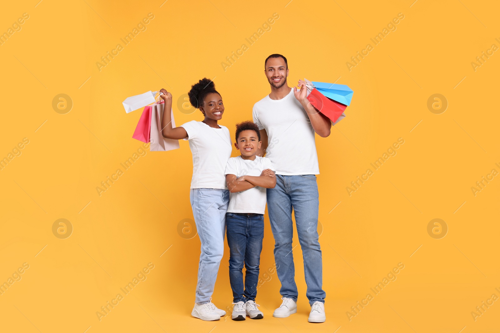 Photo of Family shopping. Happy parents and son with colorful bags on orange background