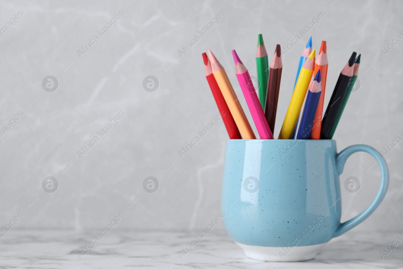 Photo of Colorful pencils in cup on white marble table against grey background. Space for text