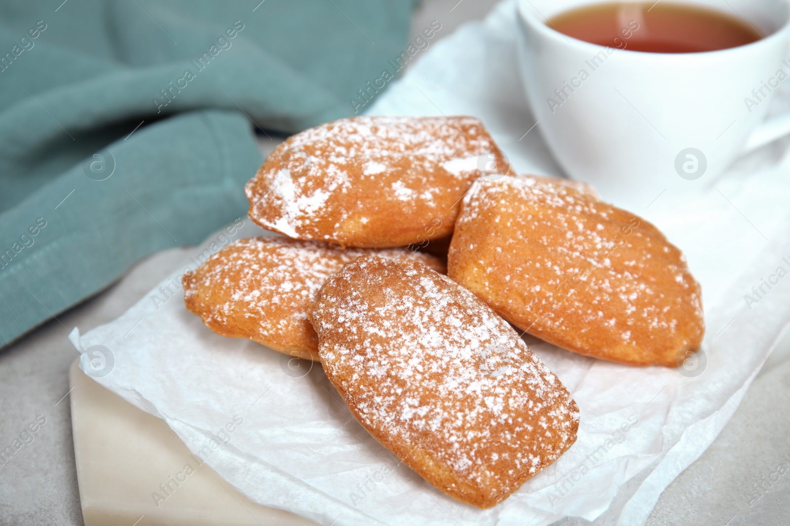 Photo of Delicious madeleine cakes with powdered sugar and tea on table, closeup