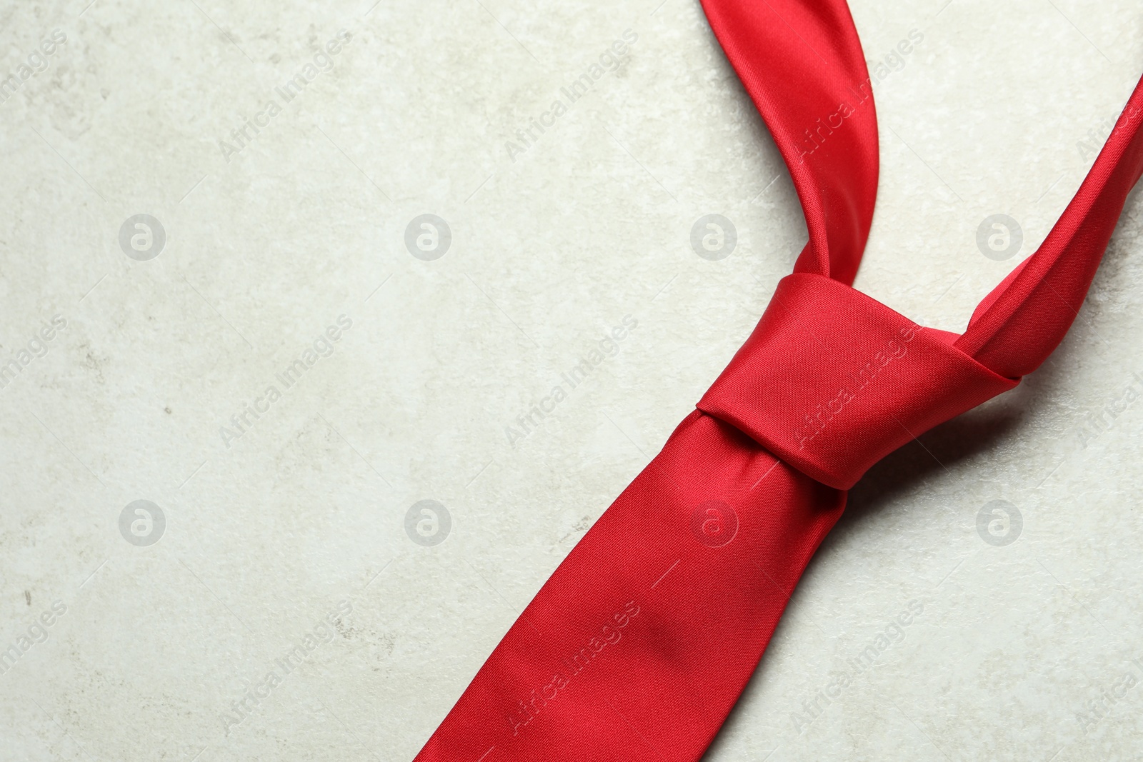 Photo of One red necktie on light textured table, top view. Space for text