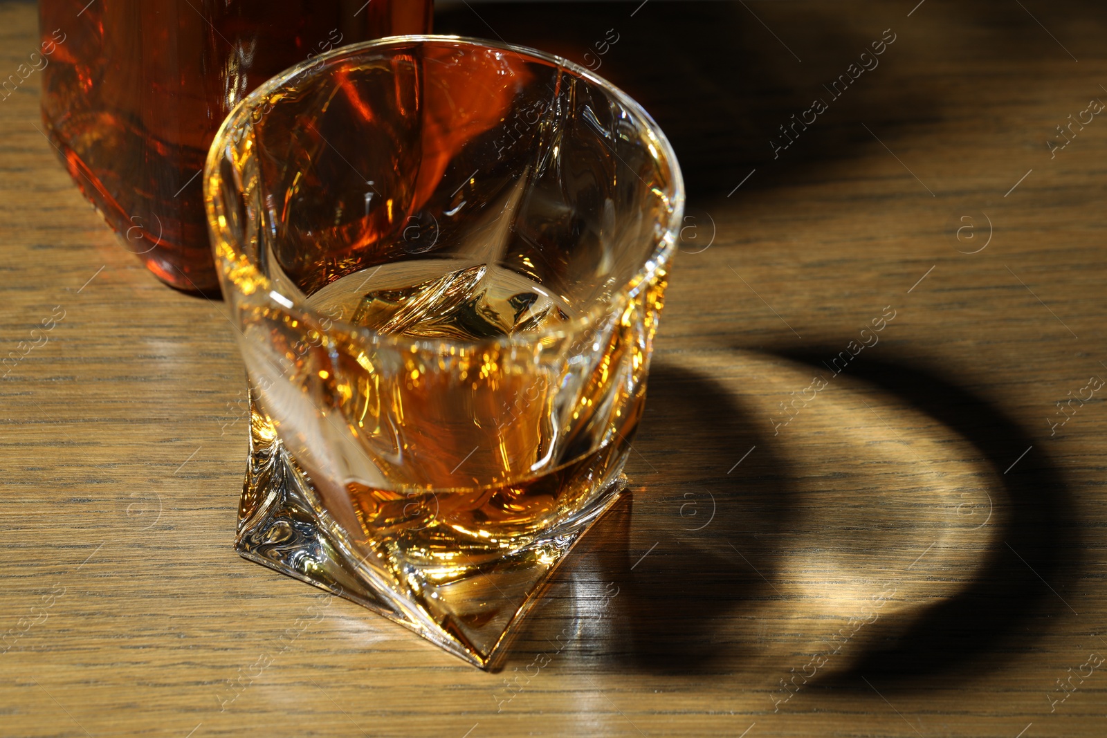 Photo of Whiskey in glass on wooden table, closeup. Space for text