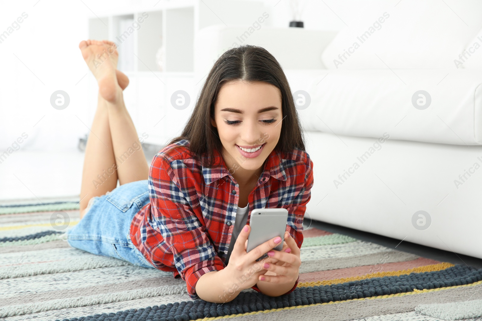 Photo of Attractive young woman using mobile phone on floor at home