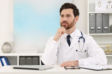 Medical consultant with stethoscope at table in clinic, space for text