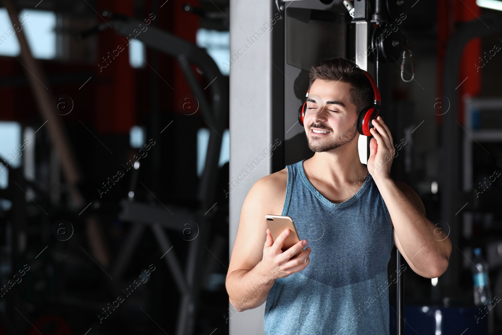 Photo of Young man with headphones listening to music on mobile device at gym