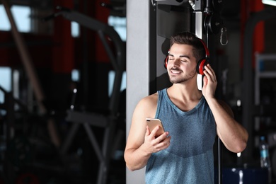 Photo of Young man with headphones listening to music on mobile device at gym