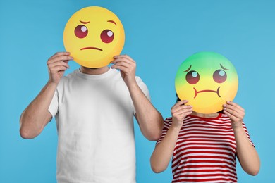 People covering faces with emoticons on light blue background