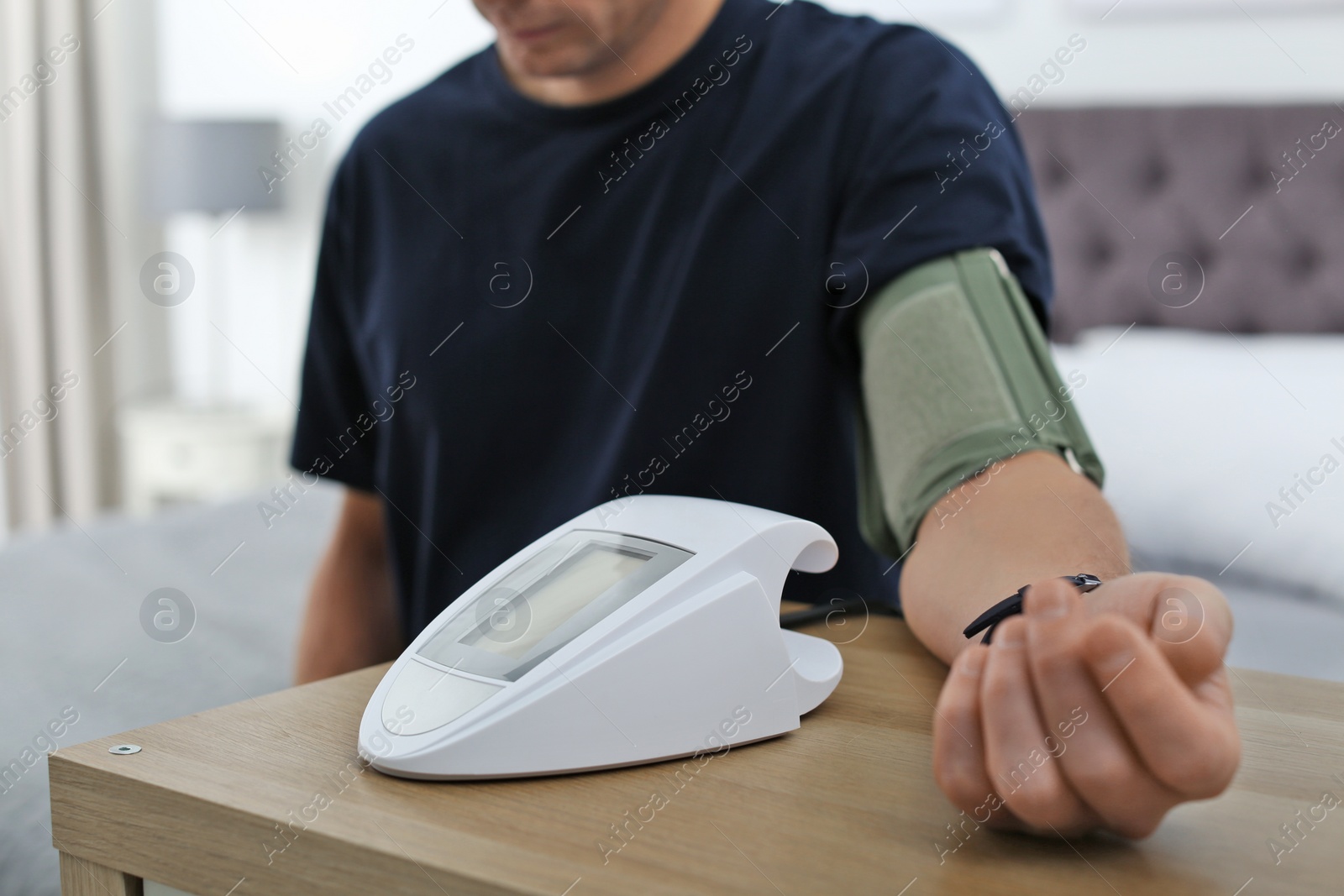 Photo of Man checking blood pressure with sphygmomanometer at table indoors, closeup. Cardiology concept