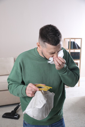Photo of Man with vacuum cleaner bag suffering from dust allergy at home