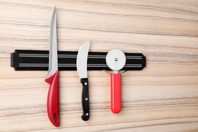 Photo of Magnetic holder with set of knives on wooden background