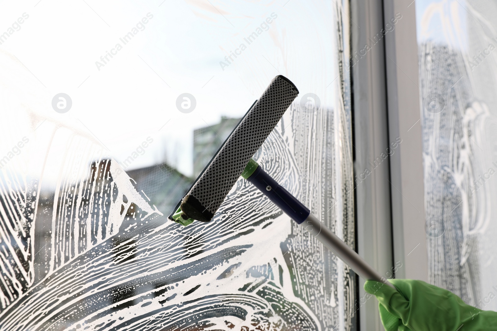 Photo of Woman cleaning window with squeegee indoors, closeup