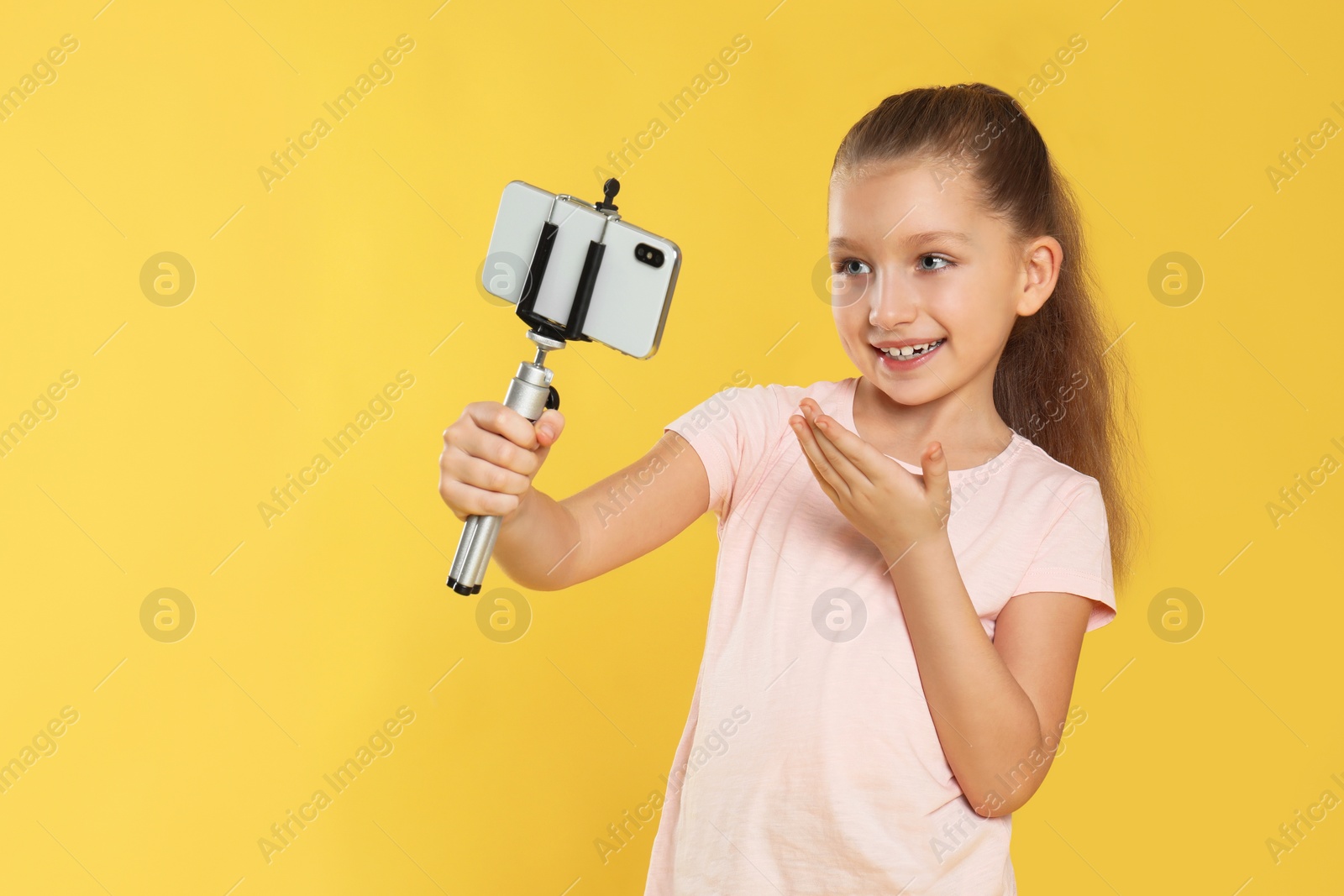 Photo of Cute little blogger recording video on yellow background