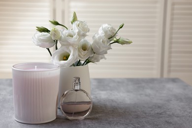 Photo of Scented candle, perfume and vase with eustoma flowers on gray marble table, space for text