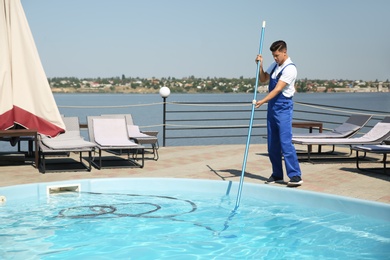 Photo of Worker cleaning outdoor swimming pool with underwater vacuum