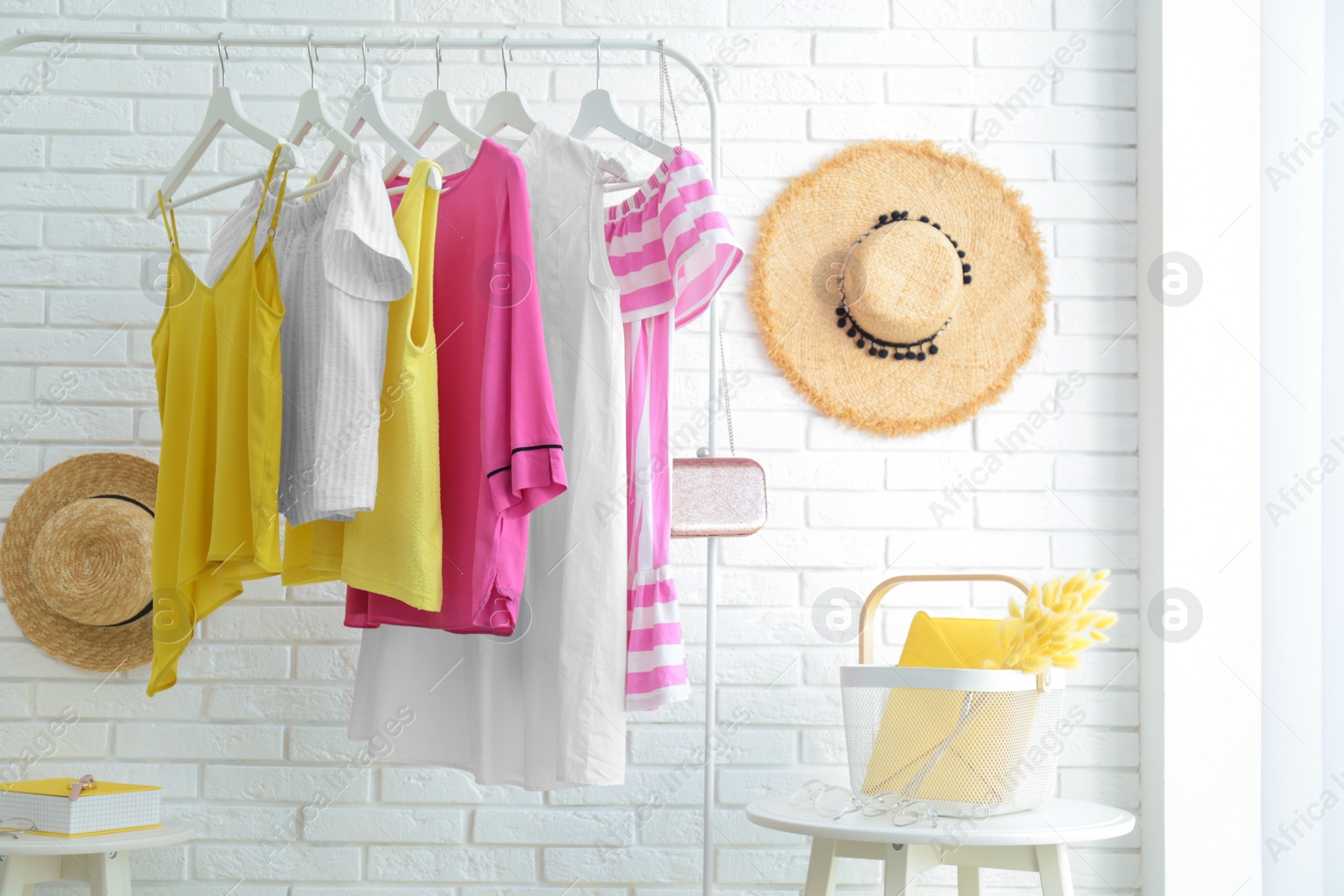 Photo of Wardrobe rack with women's clothes at white brick wall in room