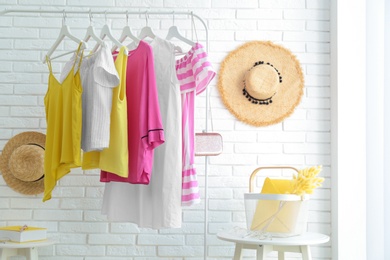 Wardrobe rack with women's clothes at white brick wall in room