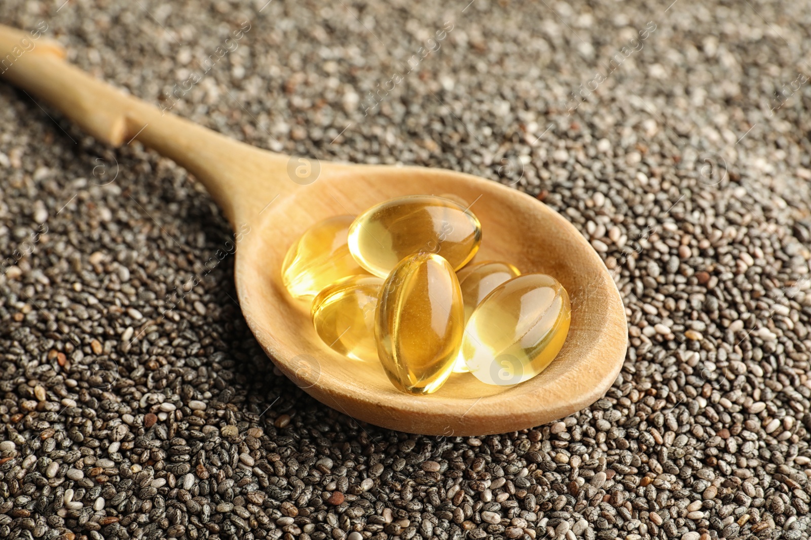 Photo of Spoon with oil capsules on chia seeds, closeup