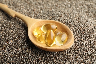 Photo of Spoon with oil capsules on chia seeds, closeup