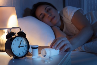 Photo of Mature woman taking bottle with pills in bedroom at night, focus on hand. Insomnia concept
