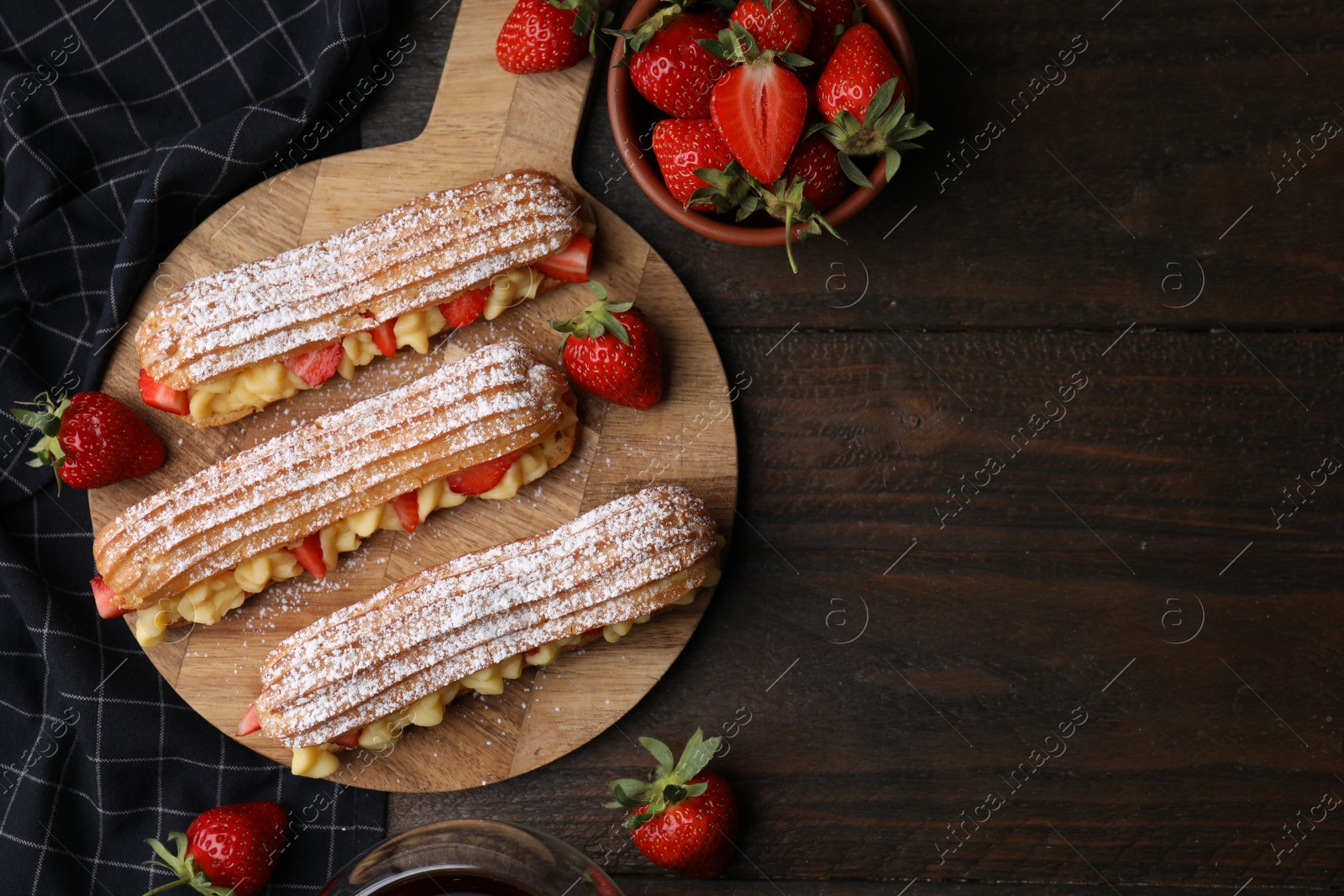 Photo of Delicious eclairs filled with cream and strawberries on wooden table, top view. Space for text