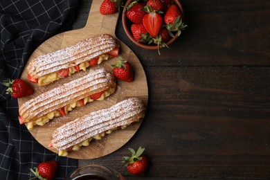 Photo of Delicious eclairs filled with cream and strawberries on wooden table, top view. Space for text