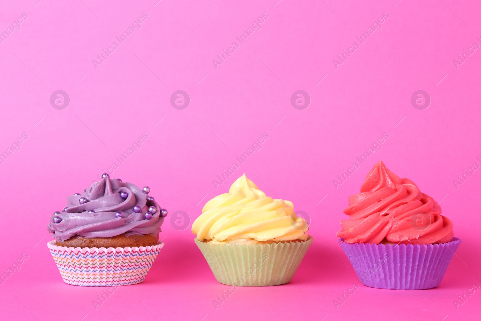 Photo of Delicious cupcakes with bright cream and sprinkles on pink background. Space for text