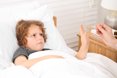 Photo of Son refusing to take cough syrup from his mother in bedroom