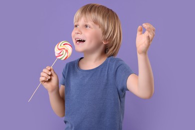 Happy little boy with colorful lollipop swirl on violet background