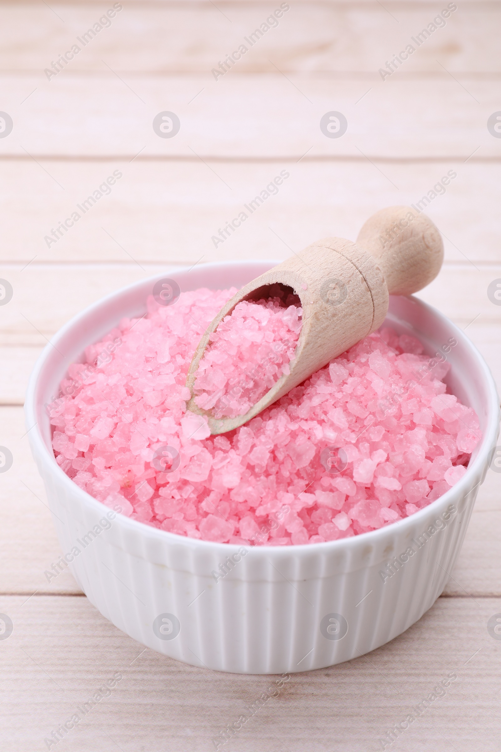 Photo of Bowl and scoop with pink sea salt on white wooden table, closeup