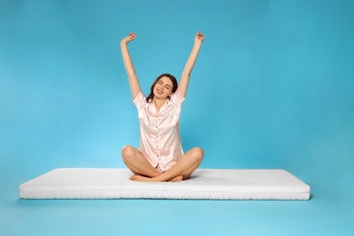 Photo of Young woman stretching on soft mattress against light blue background