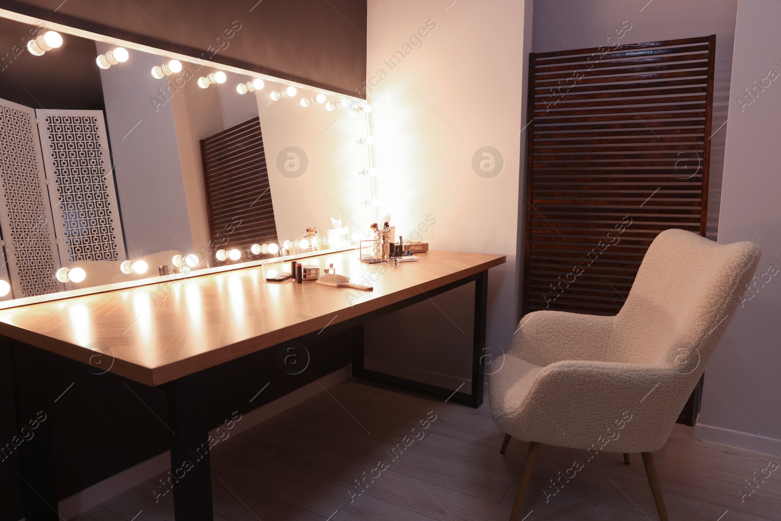 Photo of Stylish mirror with light bulbs near table with makeup products and armchair in dressing room