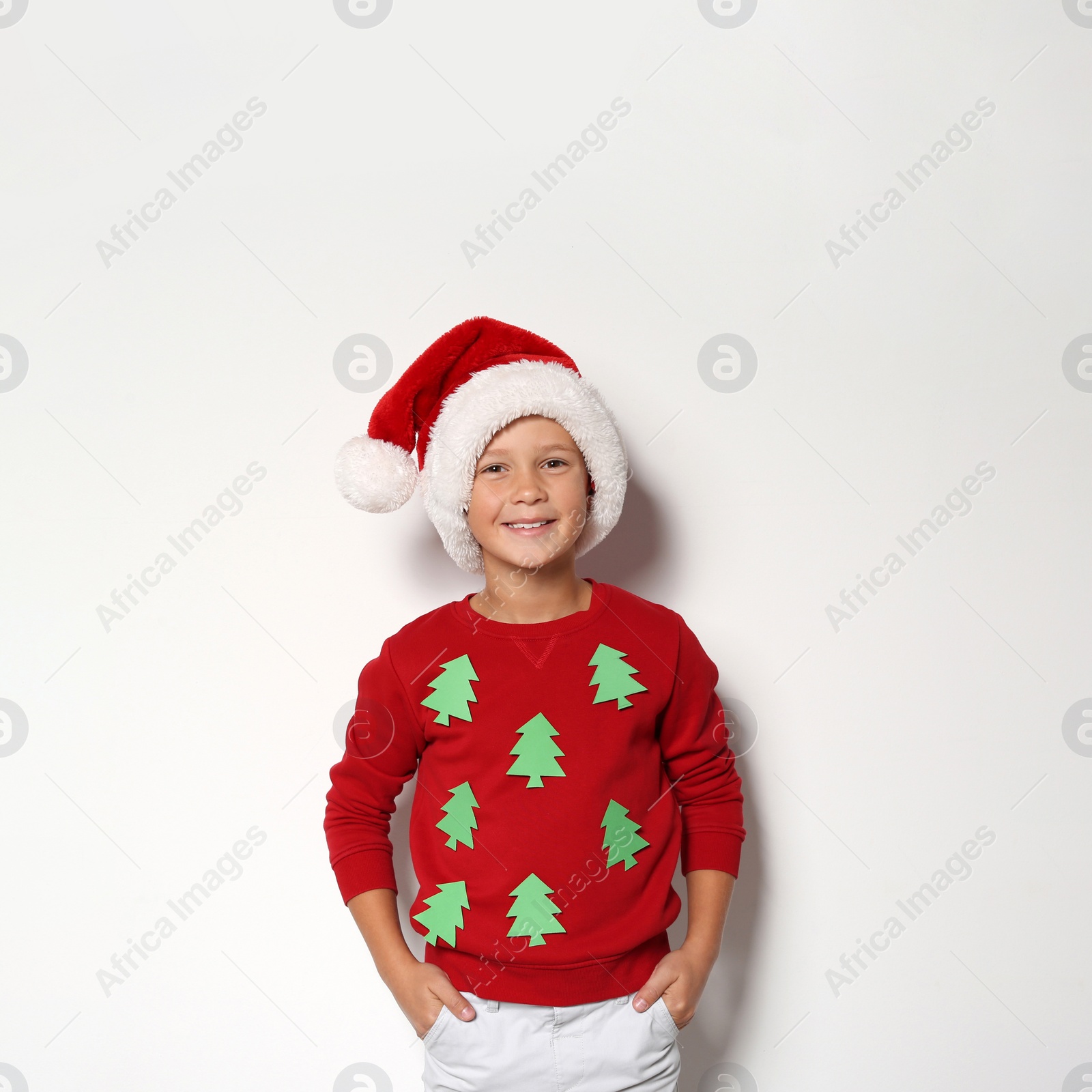 Photo of Cute little boy in handmade Christmas sweater and hat on white background