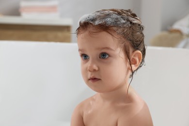 Photo of Cute little girl washing hair with shampoo in bathroom