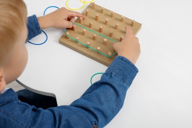 Photo of Motor skills development. Boy playing with geoboard and rubber bands at white table, closeup. Space for text