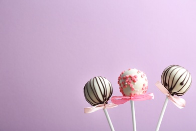 Photo of Tasty cake pops with bows on violet background. Space for text