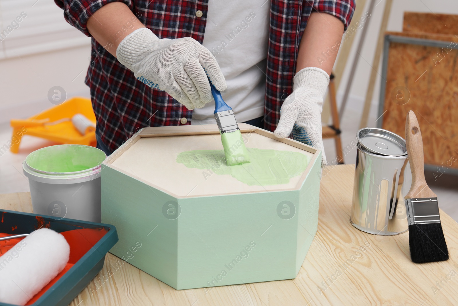 Photo of Man painting honeycomb shaped shelf with brush at wooden table indoors, closeup