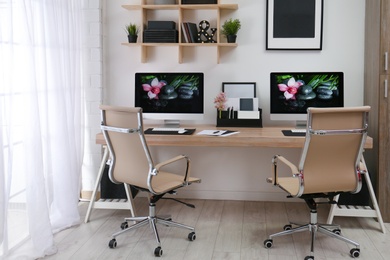 Photo of Modern workplace with large desk and computers in room. Stylish interior