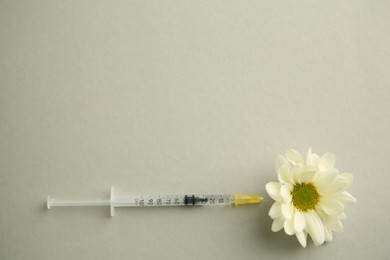Photo of Medical syringe and beautiful chrysanthemum flower on grey background, top view. Space for text