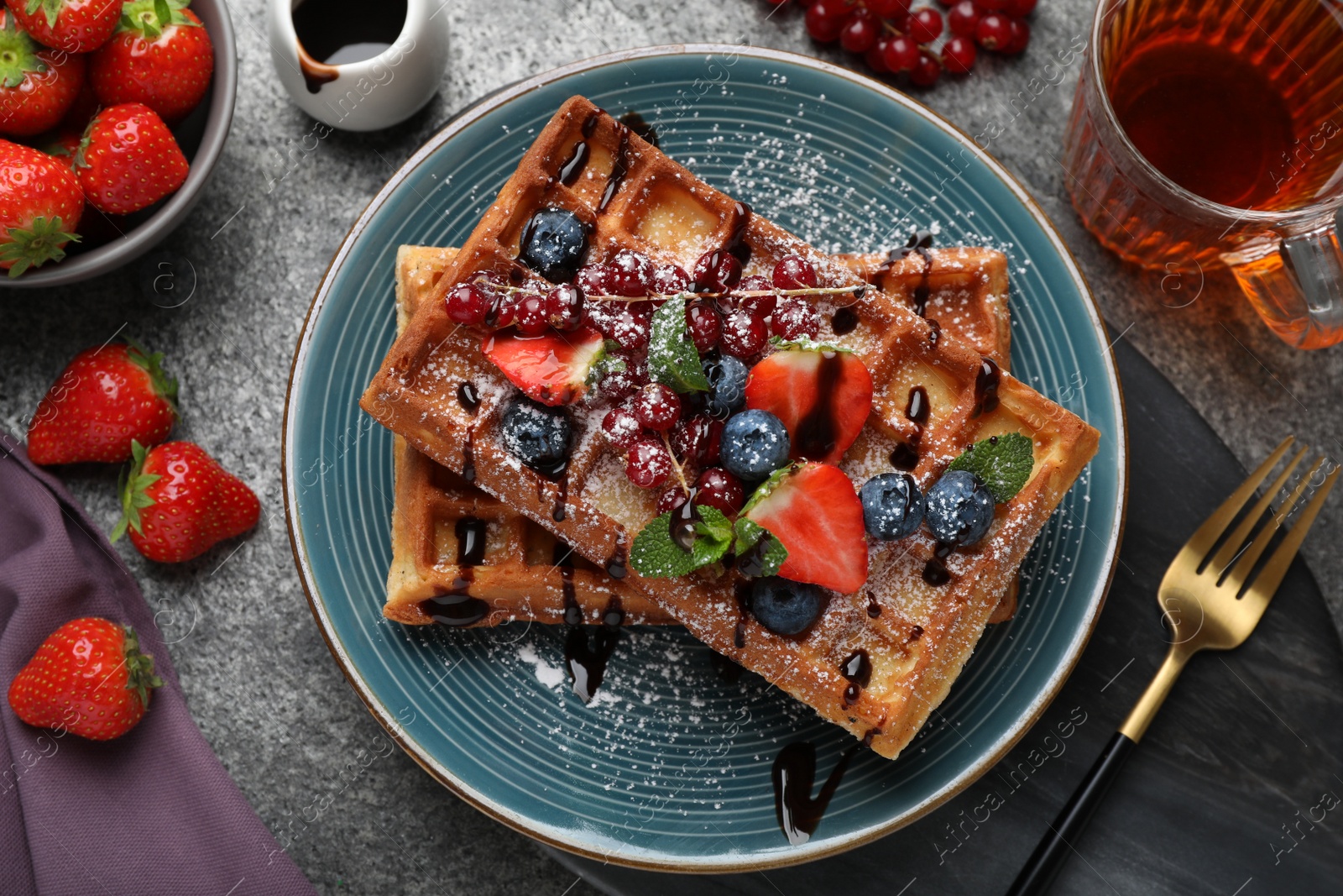Photo of Delicious Belgian waffles with berries served on grey table, flat lay