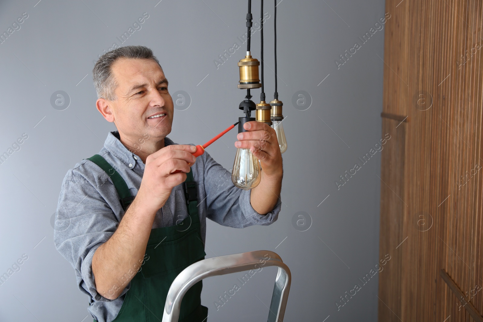 Photo of Electrician with screwdriver repairing ceiling lamp indoors. Space for text