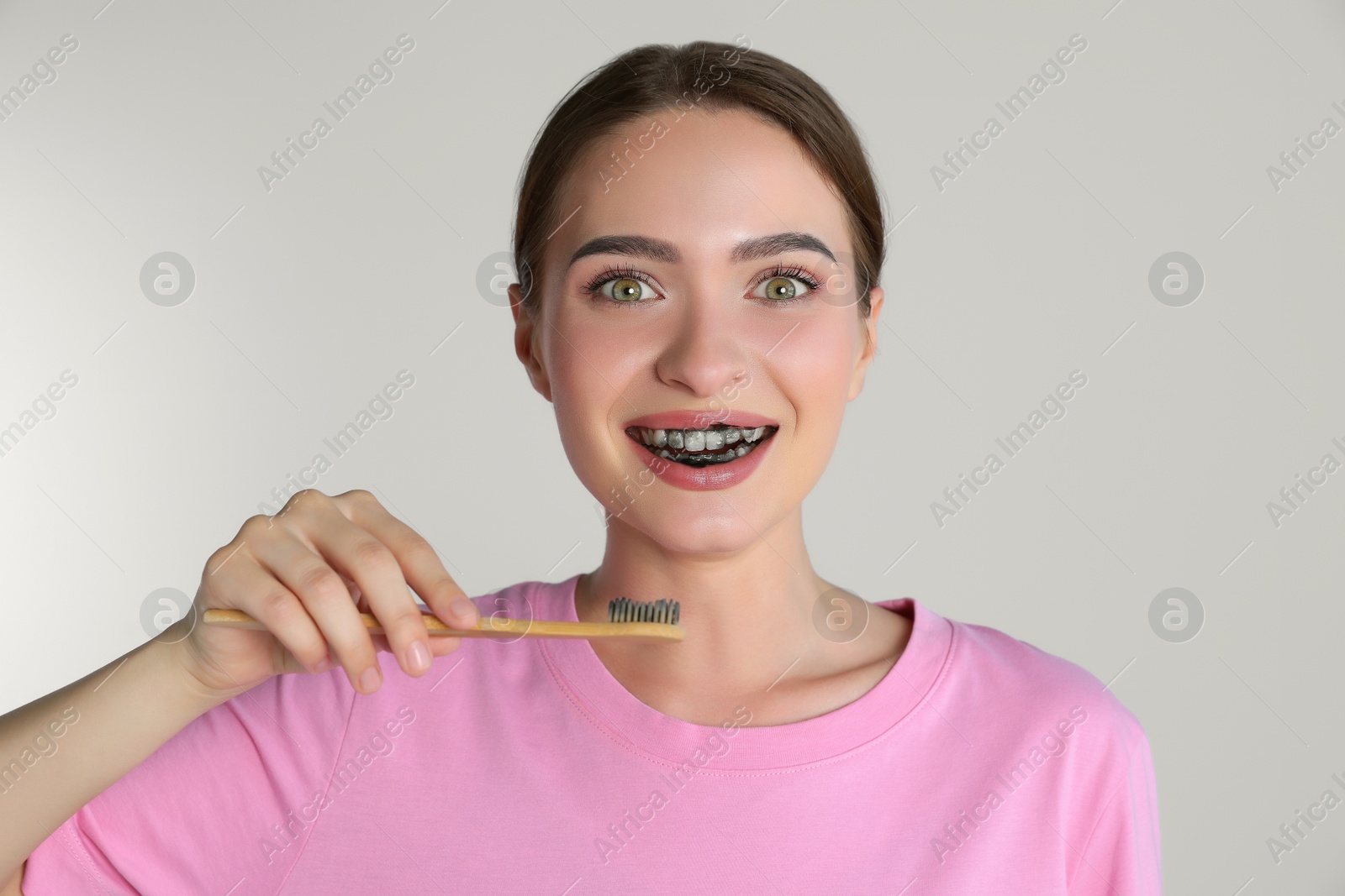 Photo of Young woman brushing teeth with charcoal toothpaste on light background