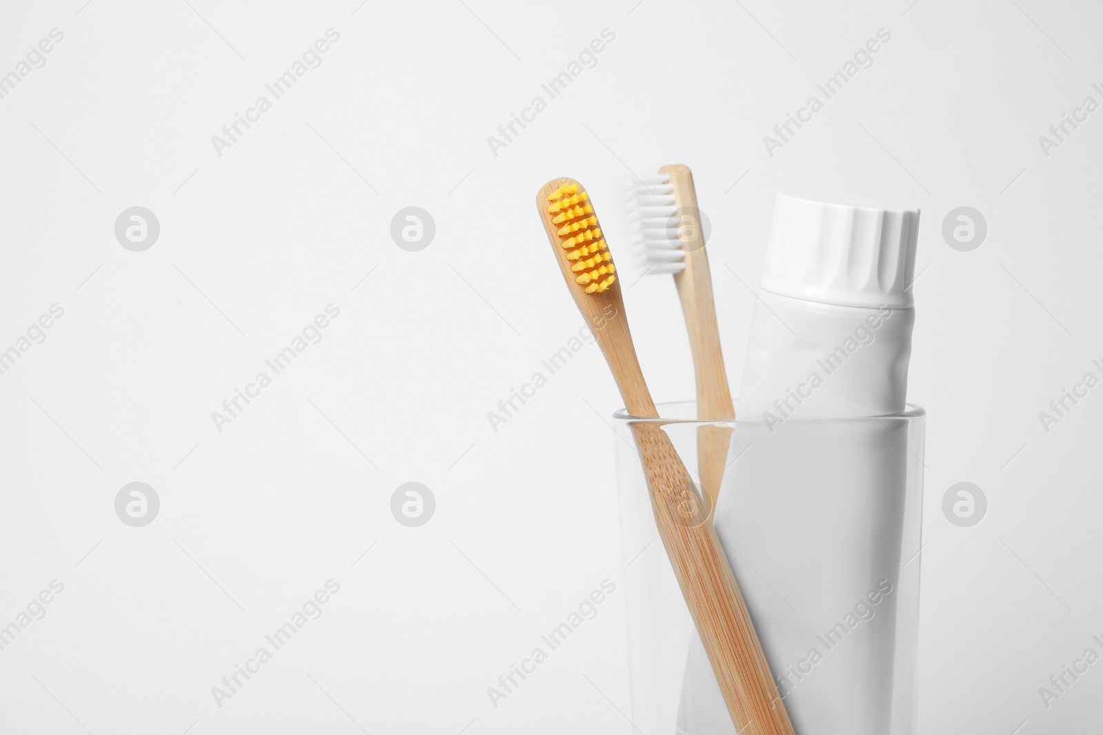 Photo of Glass with brushes and toothpaste on white background. Space for text