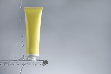 Moisturizing cream in tube on glass with water drops against grey background. Space for text